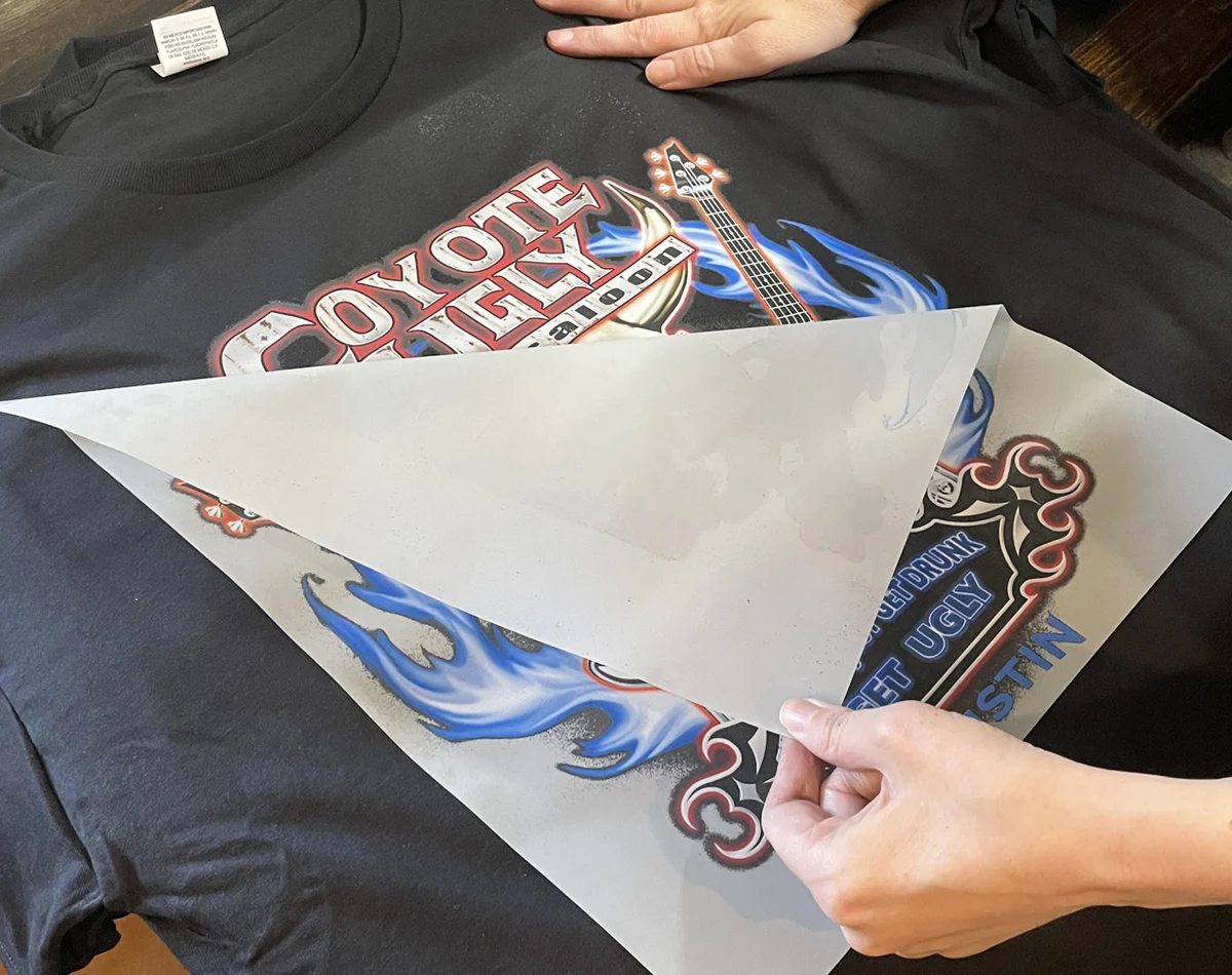 Printed DTF transfer being removed from a custom apparel design after heat application